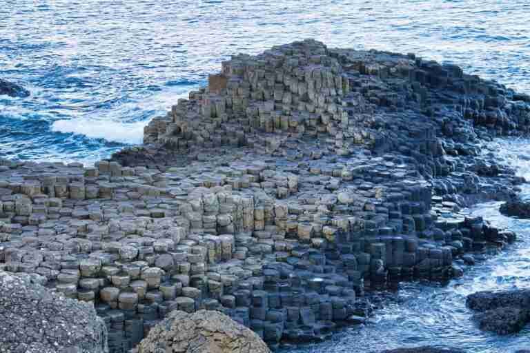 An image of the Giant's Causeway in Northern Ireland, showing hexagonal basalt columns near the sea with waves gently breaking against them.